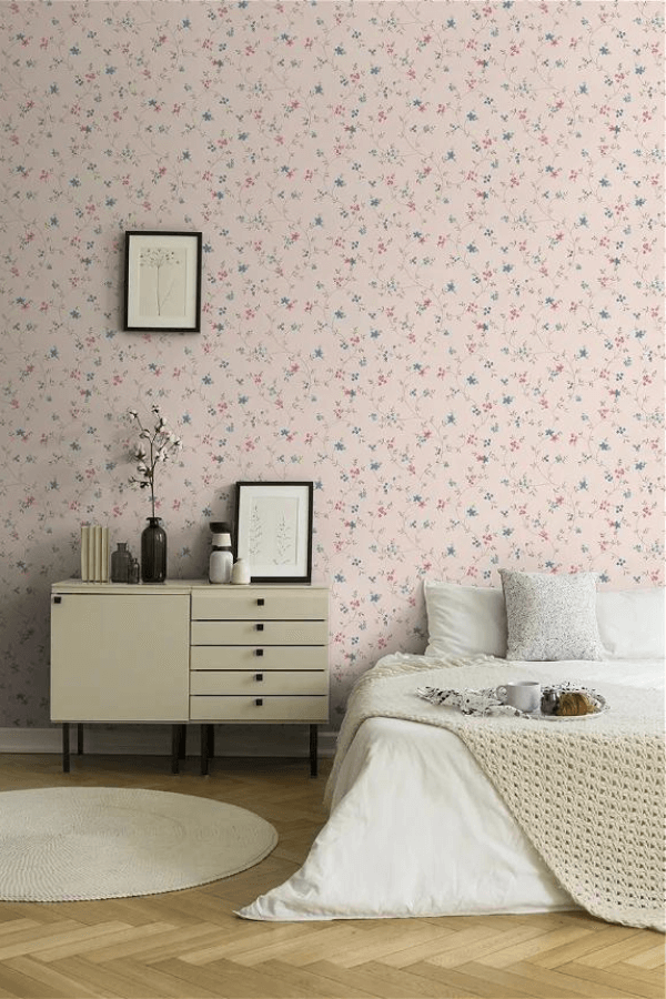 A bedroom with a color pink and floral wallpaper, bedside cabinet and a picture frames