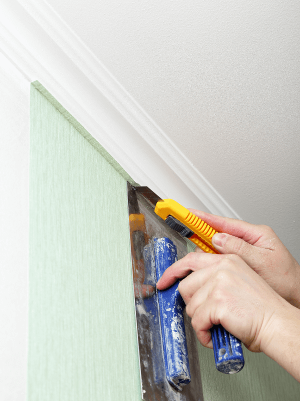 A man carefully fixing a wallpaper with a cutter and metal flat board