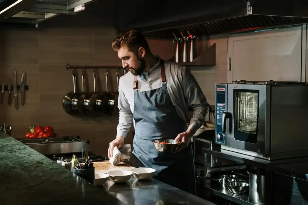 A guy wearing an apron in industrial-style-kitchen-with-pots-pans-and-appliances-on-display