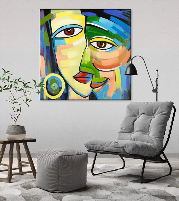 Colorful modern cubist painting of abstract faces displayed above a grey armchair in a stylish living room setting with indoor plants and minimalistic decor