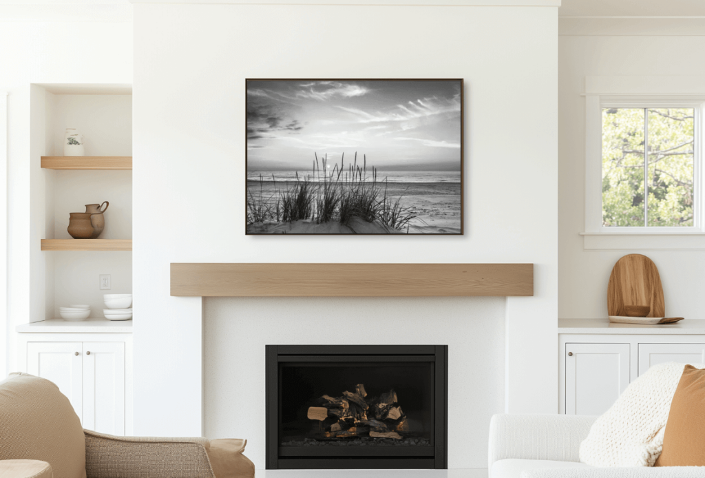 A modern living room with a black and white landscape painting above a wooden mantelpiece, with white walls and wooden accents